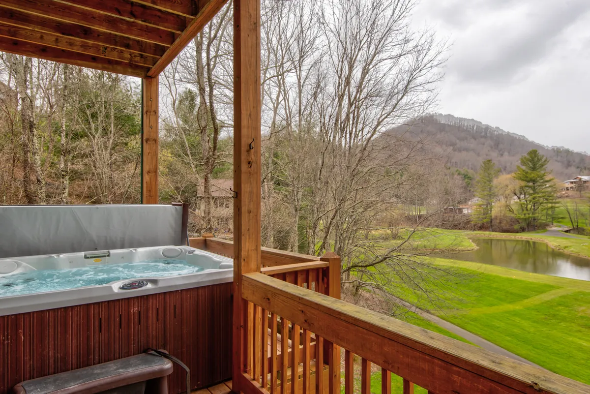 A bubbling hot tub is positioned on a private wooden deck with a railing, offering panoramic views of the landscape. The scene is tranquil, with starlit soaking and nature sounds enhancing the sense of serenity.