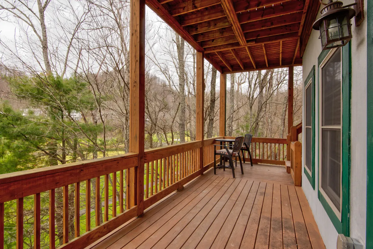 A wooden deck with comfortable outdoor seating overlooks a lush landscape of trees and rolling hills. The area is perfectly suited for sipping morning coffee, relaxing with a book, or simply enjoying the natural beauty and tranquility that surrounds the cabin. The inviting setup highlights a space for peaceful outdoor leisure.