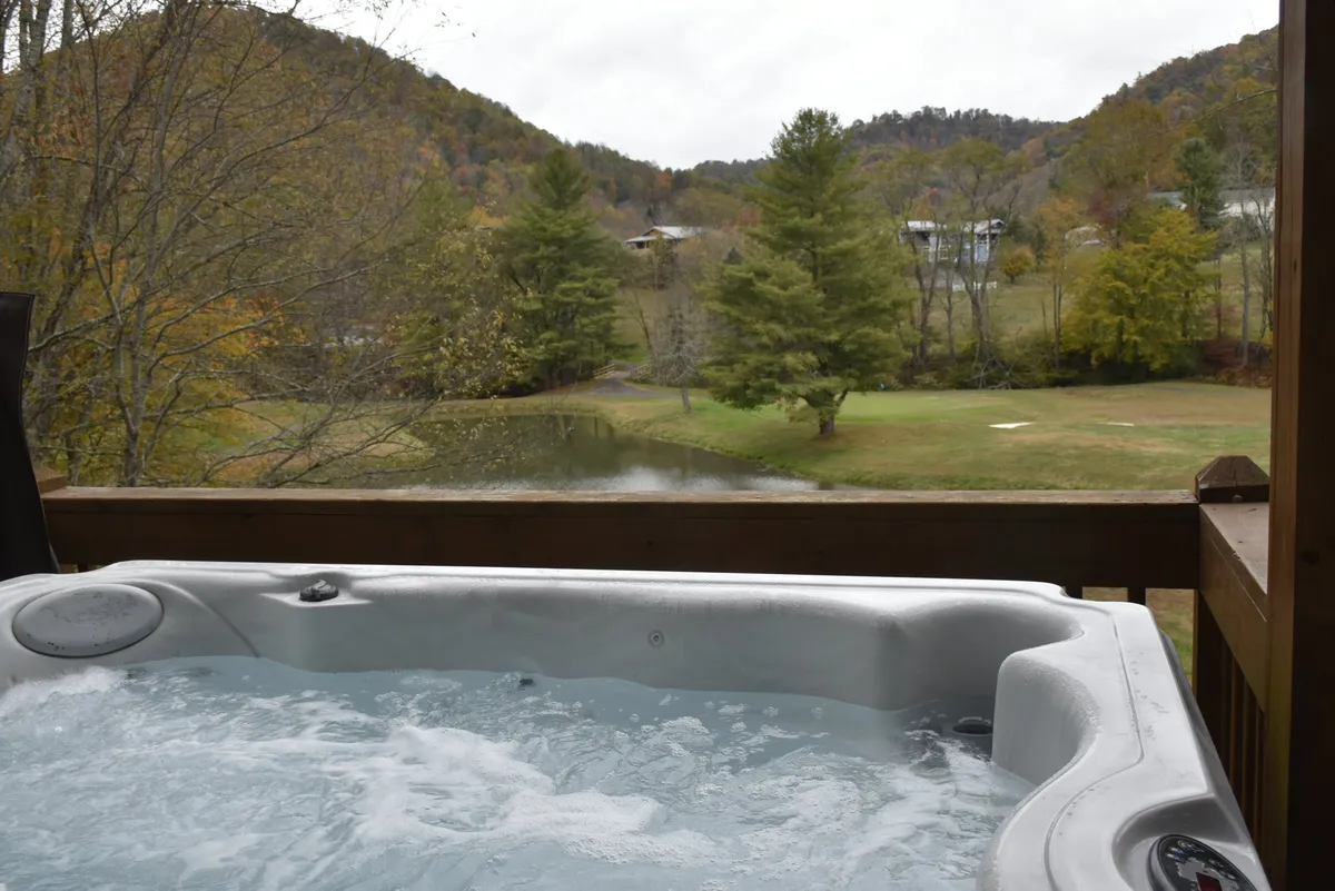 A hot tub perched on a deck overlooking a scenic pond and gentle rolling hills. The view extends toward the golf course, and the peaceful setting is framed by the colors of sunset, inviting relaxation in a tranquil setting.