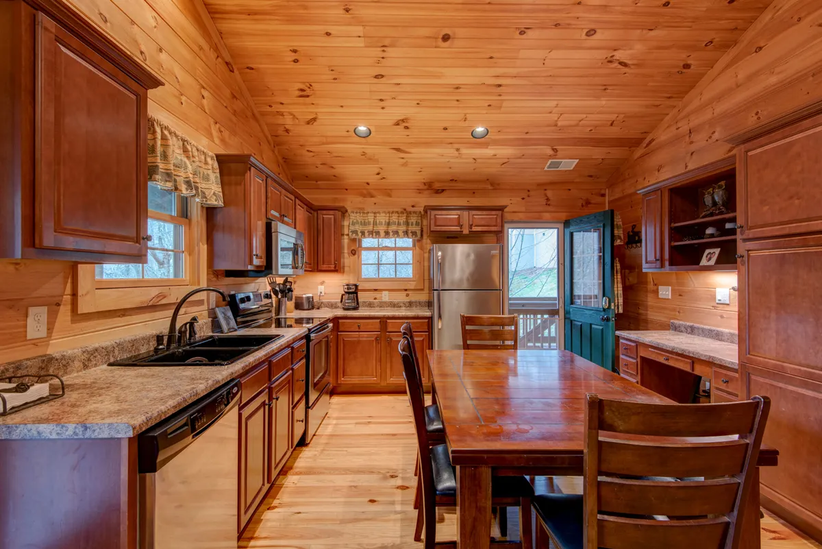 A wooden dining table at the center of an open-plan space, with the kitchen countertop, blue door, and inviting cabinetry in view. The scene is set for family meals, with ample space for group dining and lively conversation.