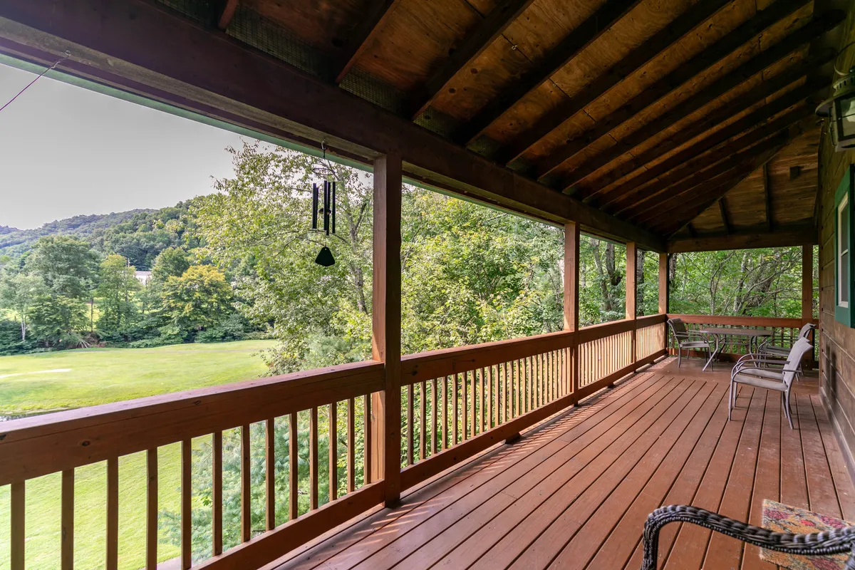 A spacious wooden deck with inviting outdoor seating, overlooking lush greenery and sweeping mountain views. Wind chimes dangle from the roof, and the deck is bathed in soft natural light—an ideal spot for sipping morning coffee or enjoying evening sunsets.