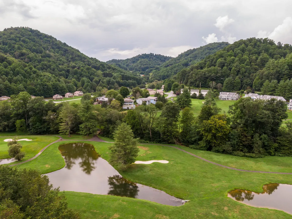 This scenic view highlights rolling hills, a golf course, tranquil ponds, and neighboring homes. The landscape is bathed in serene light, ideal for outdoor exploration and activities.
