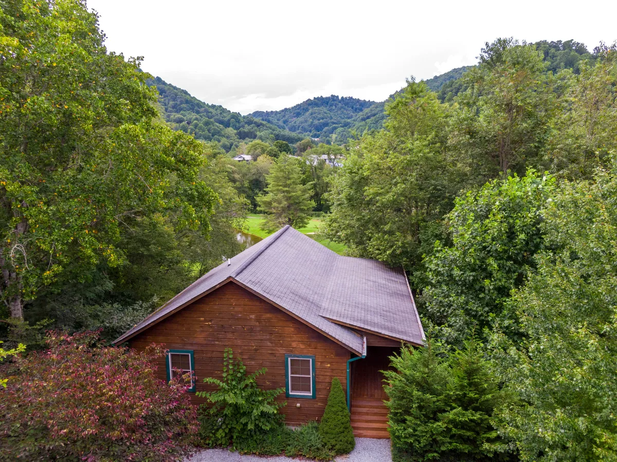 A wooden house nestled among trees with a striking mountain backdrop, evoking the sense of being immersed in nature. The setting suggests easy access to hiking trails and peaceful outdoor relaxation, with the house appearing as a gateway to adventure.