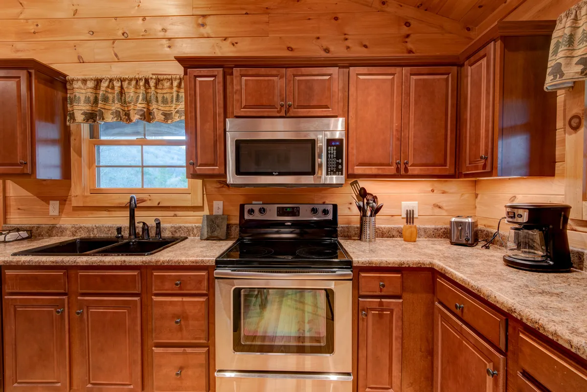 A bright, welcoming kitchen area featuring stainless steel appliances, wooden cabinetry, and a spacious countertop. The setup invites group meal prep, baking, or casual breakfasts, with a homey yet modern feel.