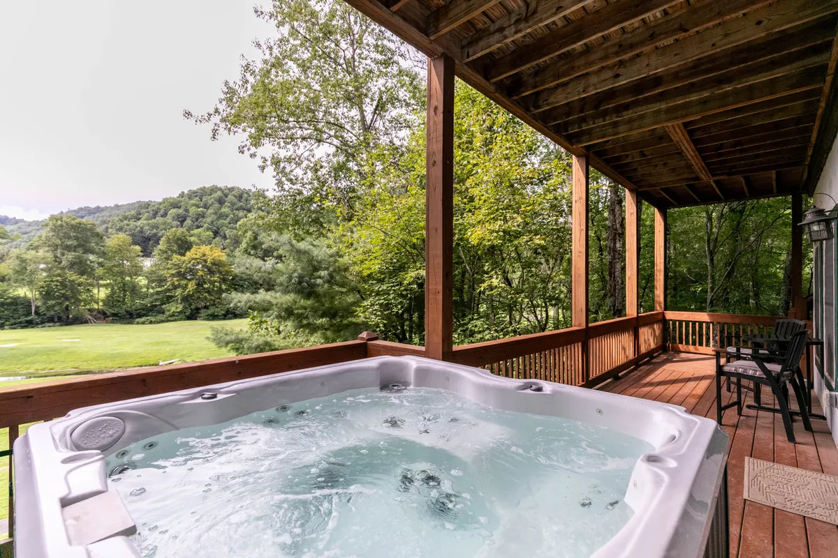 An inviting hot tub sits on a spacious wooden deck nestled among green trees. The deck offers ample space for socializing or solitude, with the hot tub positioned to maximize views of the surrounding landscape. The tranquil scene is ideal for both stargazing and morning relaxation.