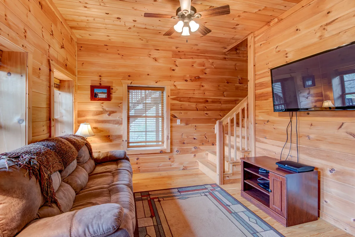 A family room with a comfortable couch, TV, and wooden walls, next to a staircase. The room feels spacious and inviting, poised for relaxation, movie nights, or family gatherings.