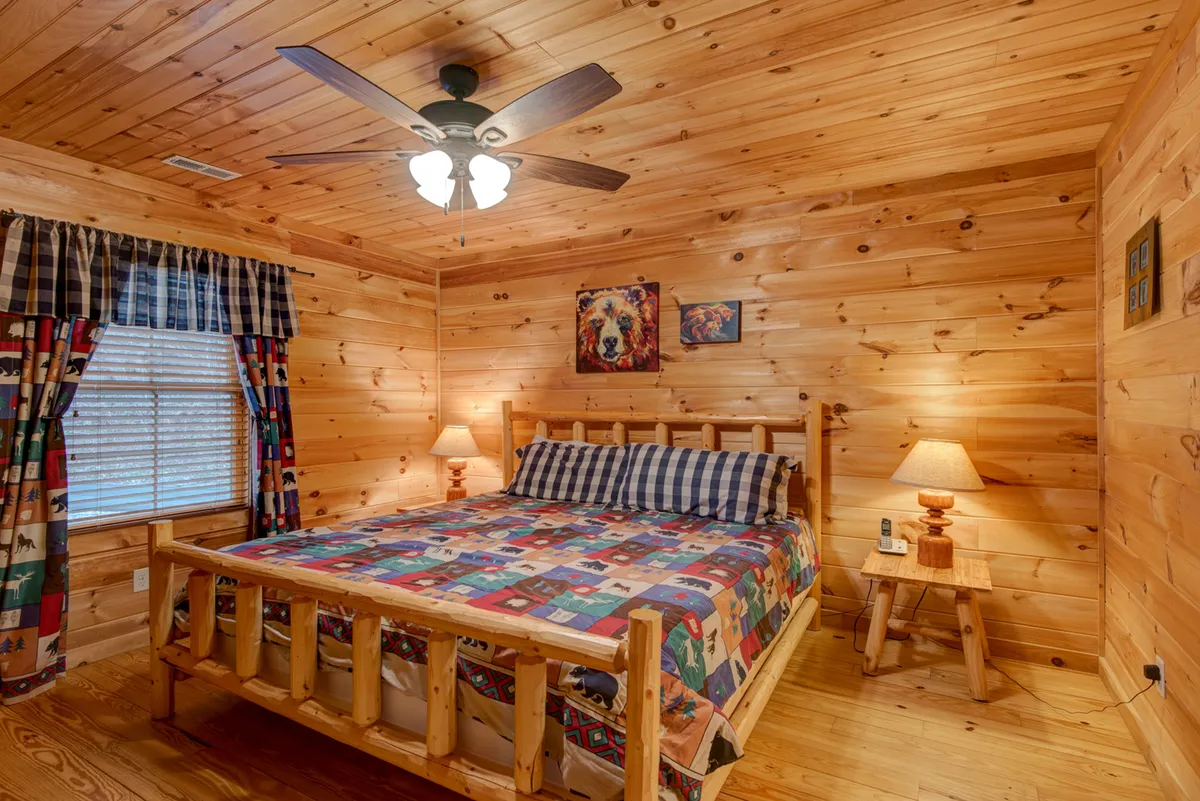A comfortable bedroom with a wooden bed adorned with a colorful quilt, a window with curtains letting in natural light, and nightstands with lamps. The room feels peaceful and welcoming, ideal for both people and pets to unwind.