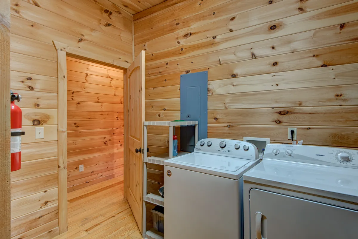 A functional laundry area featuring a washing machine and dryer set against warm wooden walls, with a doorway leading to another room. The space is clean, practical, and inviting, suggesting ease of use for guests managing dirty boots or pet-related messes after outdoor adventures.